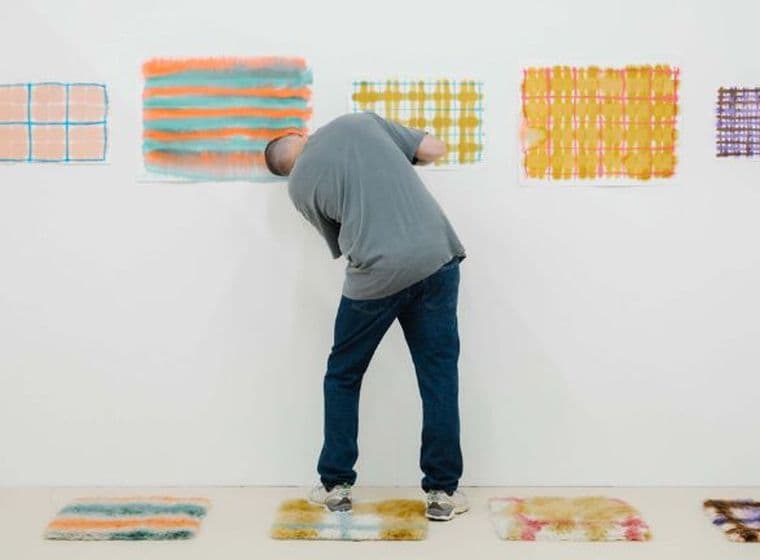 Une personne contemple des œuvres d'art abstraites colorées accrochées à un mur blanc dans une galerie, tandis que des œuvres similaires sont exposées au sol.