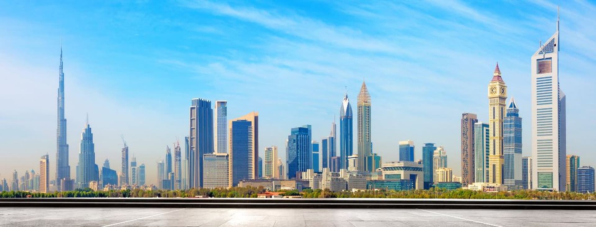Panoramic view of Dubai skyline with tall skyscrapers under a clear blue sky, featuring a prominent tower on the left.