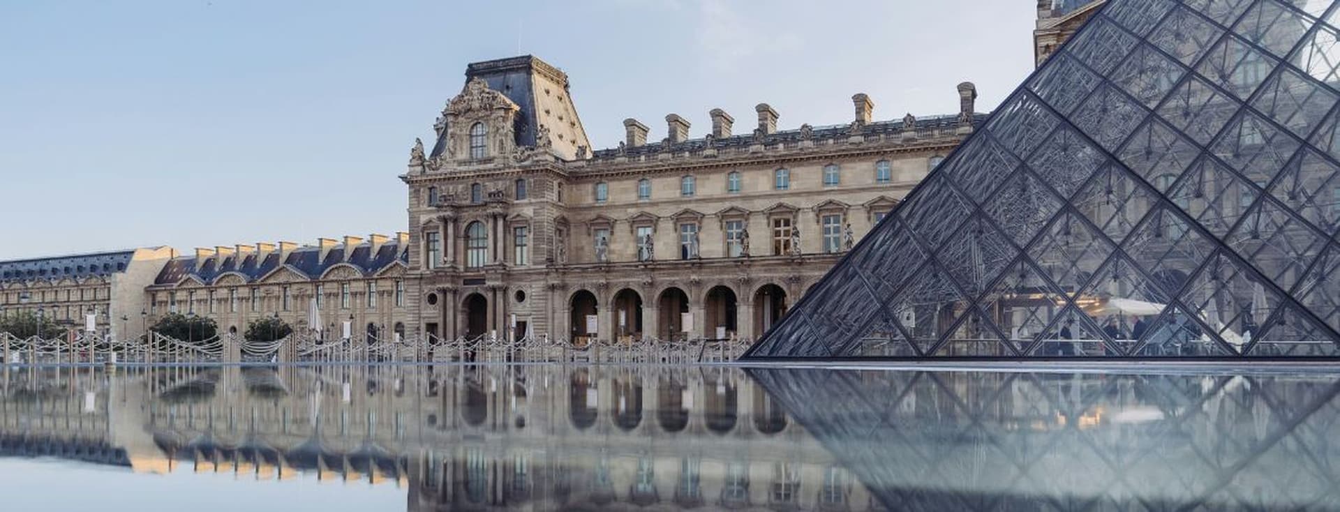 The Louvre Museum and glass pyramid reflected in water on a clear day, showcasing classical architecture and modern design.