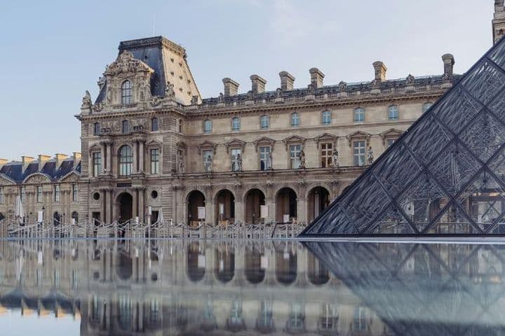 The Louvre Museum and glass pyramid reflected in water on a clear day, showcasing classical architecture and modern design.