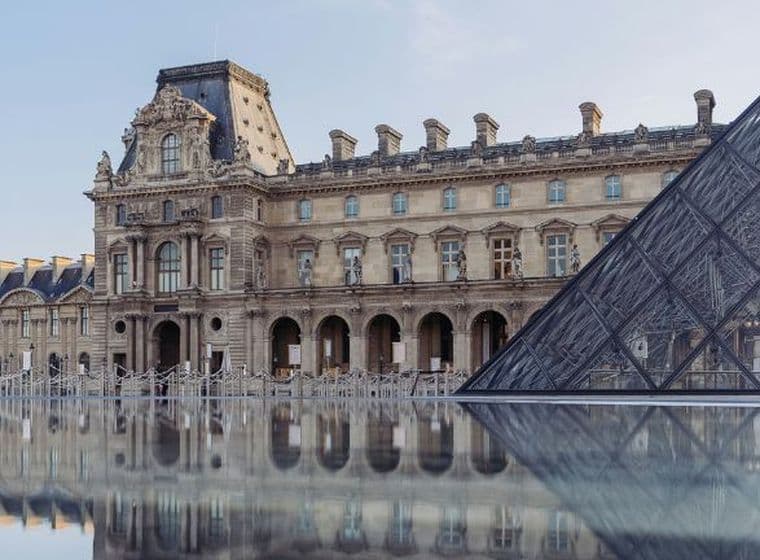 The Louvre Museum and glass pyramid reflected in water on a clear day, showcasing classical architecture and modern design.