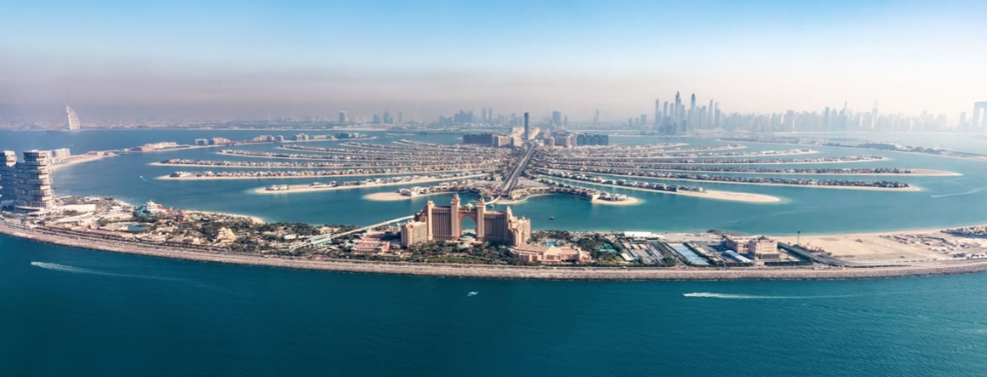 Aerial view of Palm Jumeirah, Dubai, with its palm-shaped islands, surrounded by blue waters and city skyline in the background.