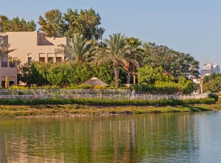 A serene view of villas in Arabian Ranches, surrounded by lush greenery and a tranquil lake, with a man walking along the water’s edge, representing one of Dubai’s best villa communities for luxurious living.