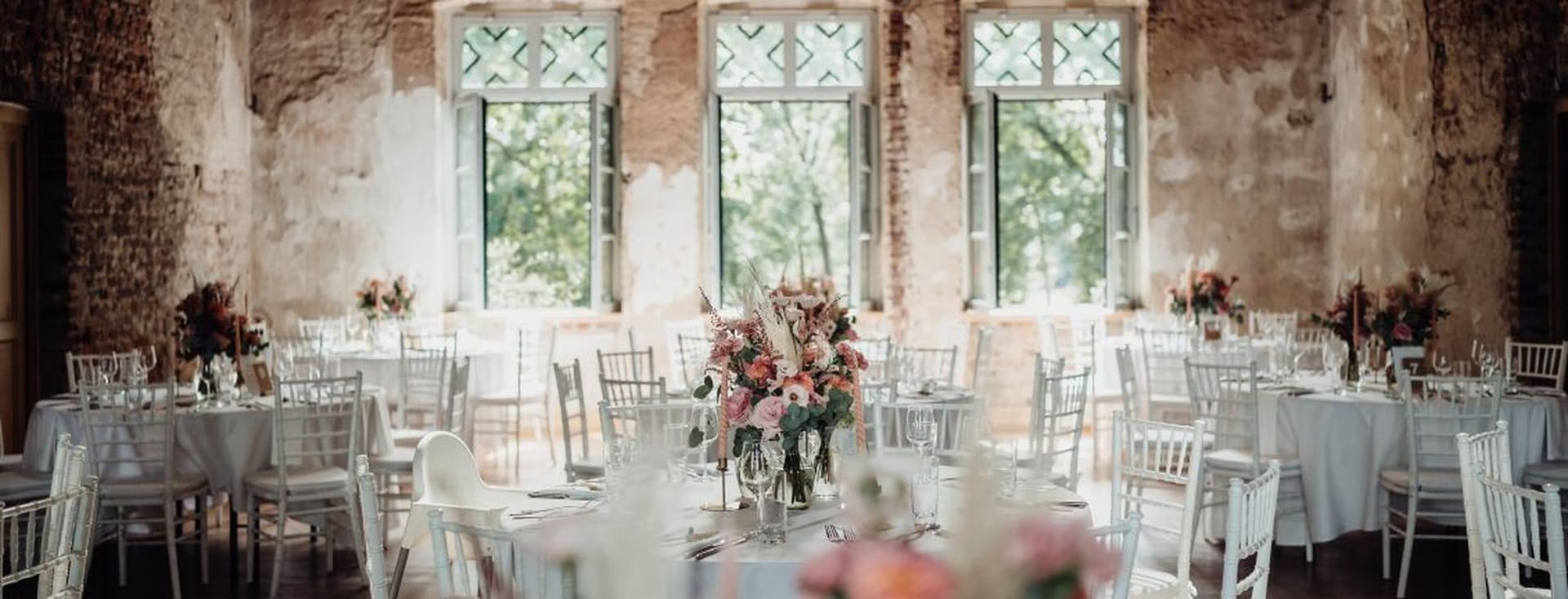 Festlich dekorierter Veranstaltungsraum in einem historischen Gebäude mit unverputzten Wänden und Holzbalkendecke, ideal für Hochzeiten und exklusive Events.