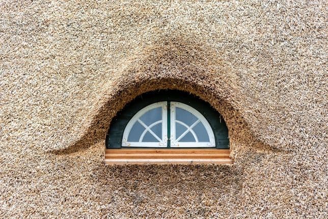 A crescent-shaped dormer in a detailed thatched roof. highlights high-quality craftsmanship and unique character of a property.