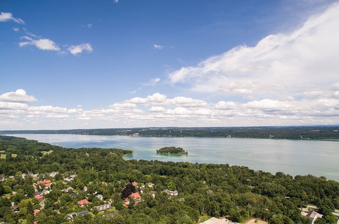 Bird’s-eye view of Feldafing with houses, forest, Lake Starnberg and Rose Island under a clear sky