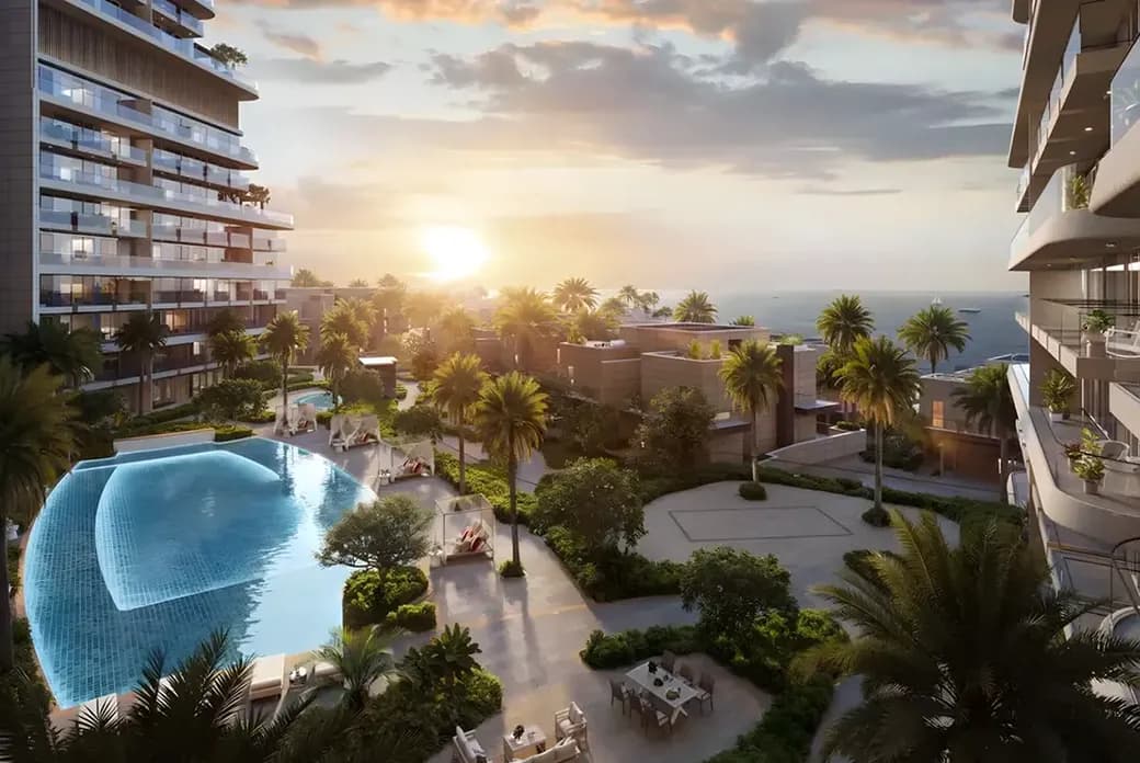 Sunset view of a modern seaside residential complex with a curved infinity pool, palm trees, balconies and ocean in the distance.
