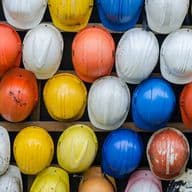 A wall of colorful hard hats, including white, yellow, orange, green, and blue, are neatly arranged on wooden shelves.