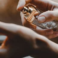 A person sprays perfume onto their wrist, with a focus on the bottle and hands.