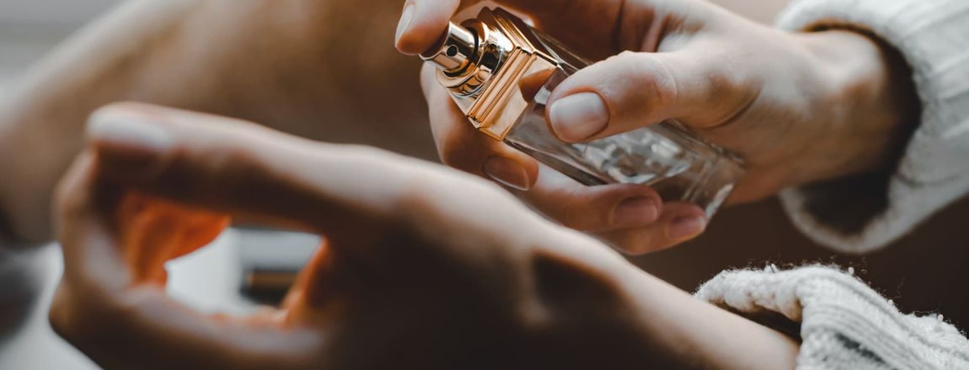 A person sprays perfume onto their wrist, with a focus on the bottle and hands.