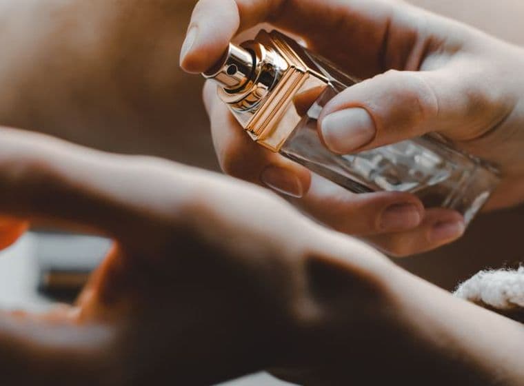 A person sprays perfume onto their wrist, with a focus on the bottle and hands.