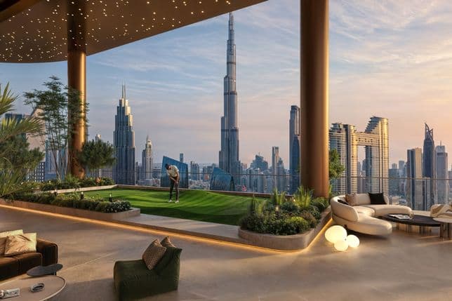Rooftop terrace with seating, a small putting green, plants, and a city skyline view at sunset, featuring a prominent, tall building.