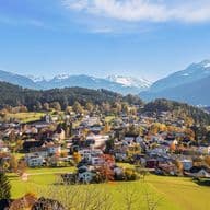 A picturesque village nestled in a valley with colorful houses, surrounded by lush greenery and snow-capped mountains under a clear blue sky.