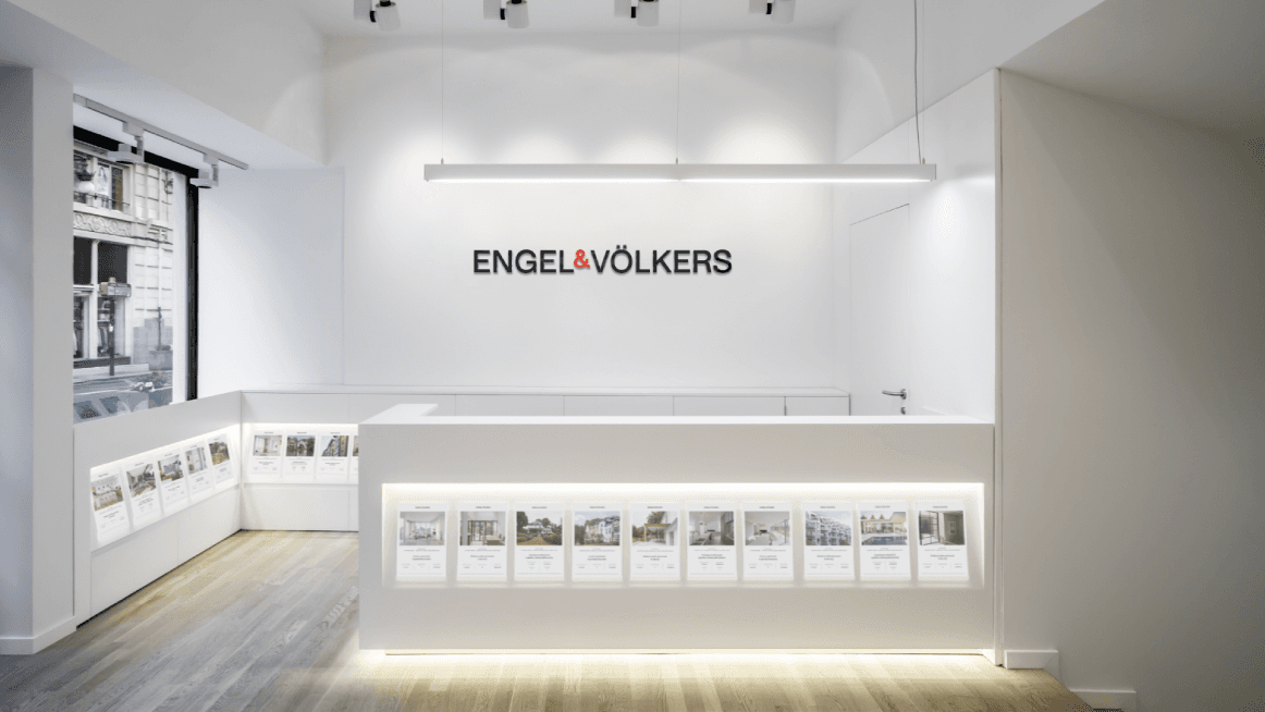 Engel & Völkers oficina immobiliària amb un taulell de recepció blanc i llistats de propietats mostrats.