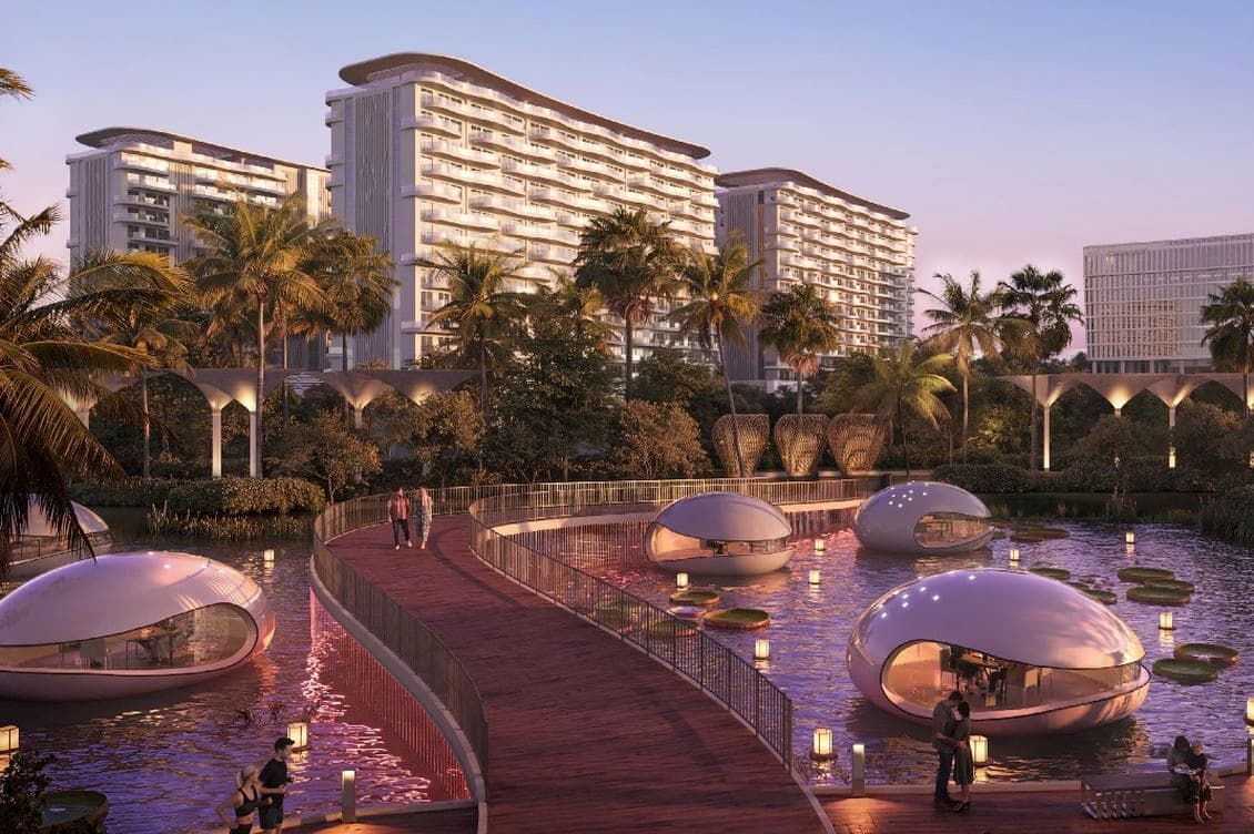 Twilight scene of a curved wooden boardwalk over a pond with futuristic glass pods, palm trees, and modern high-rise buildings in the background.