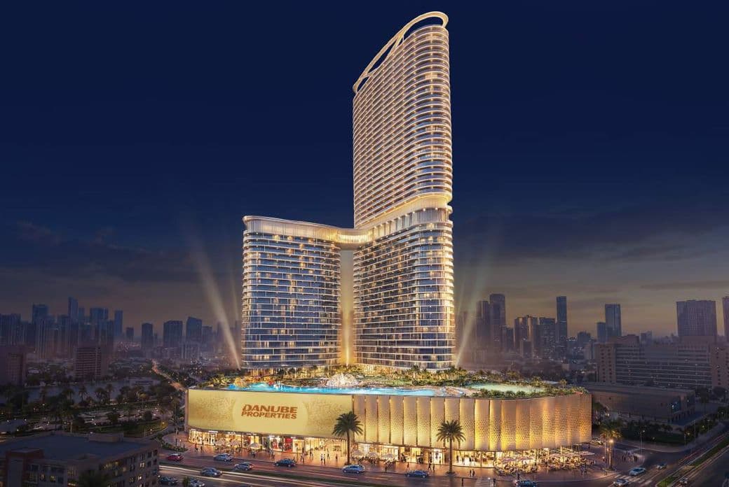 Illuminated high-rise building at night, with multiple levels, luxury design, and palm trees in front. City skyline visible in the background.