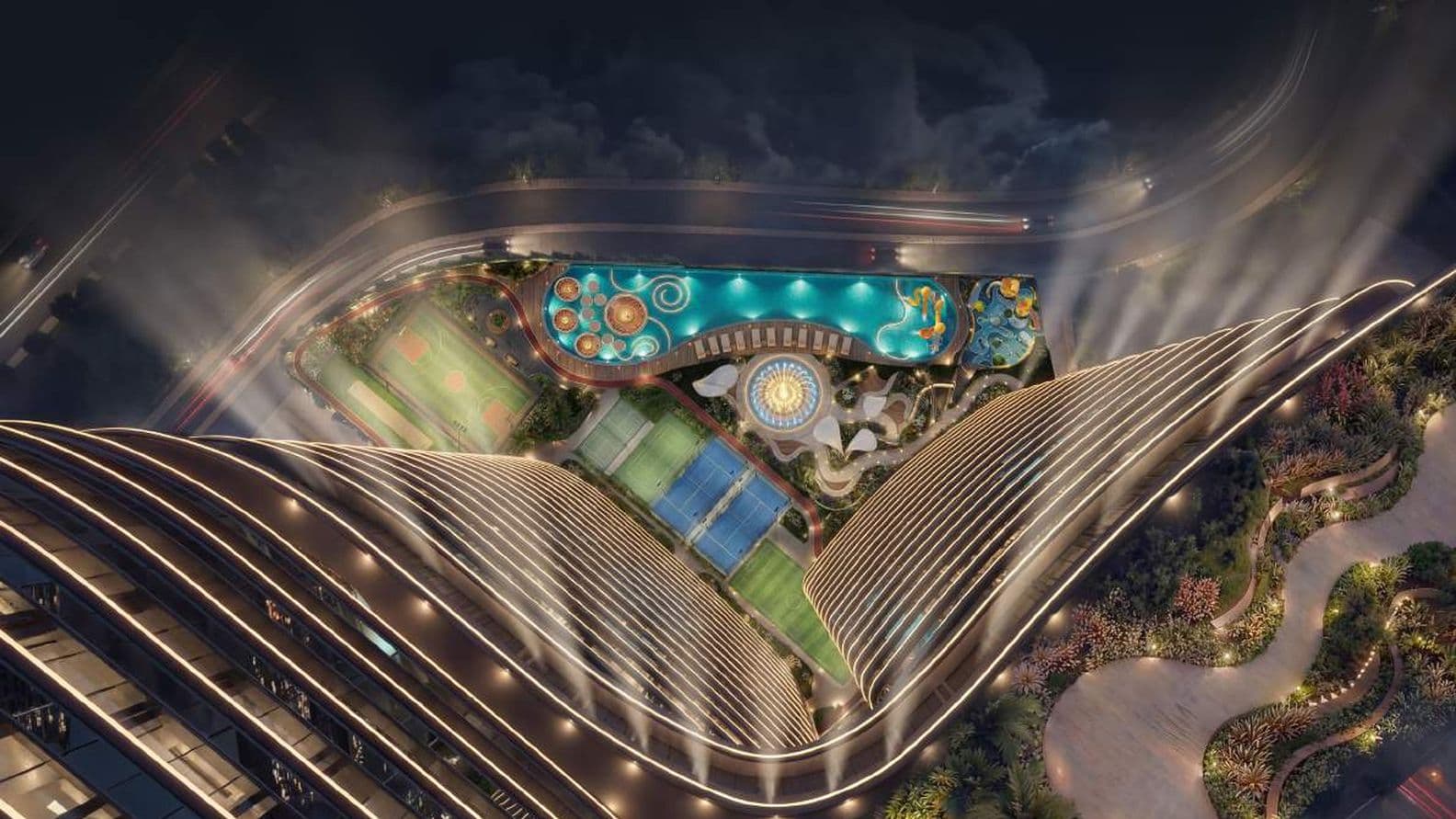 Aerial view of a luxurious skyscraper's rooftop featuring illuminated pools, tennis courts, a fountain, and surrounding greenery at night.