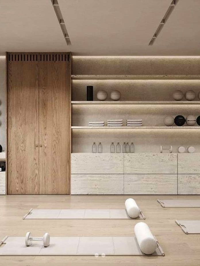 Minimalist yoga studio with wooden cabinets, shelves holding towels and equipment, and mats with bolster pillows on a light wood floor.