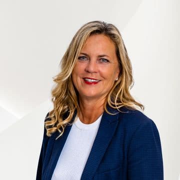 Smiling woman with long blonde hair in a blue blazer and white top, set against a light background.