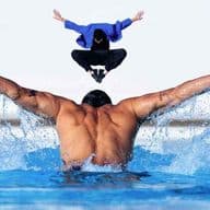 A muscular man swims butterfly in a blue pool, water splashing. Above him, a person in a blue jacket jumps. White building in background.