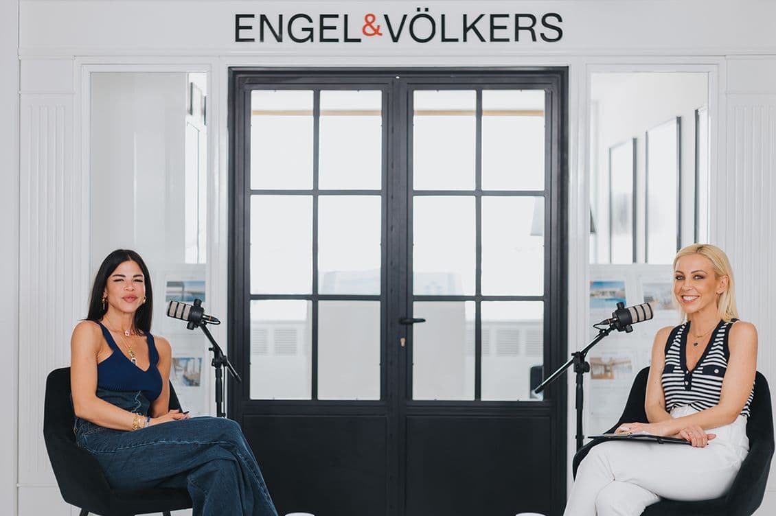 Dafni Karavokyri and Lili Piraki seated with microphones in a modern studio setting, under the Engel & Völkers sign, smiling and engaged in conversation.