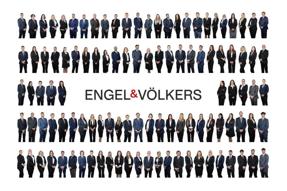 Group photo of the entire Engel & Völkers team. Dozens of men and women in business suits stand in several horizontal rows against a white background, with the Engel & Völkers logo prominently displayed in the center.