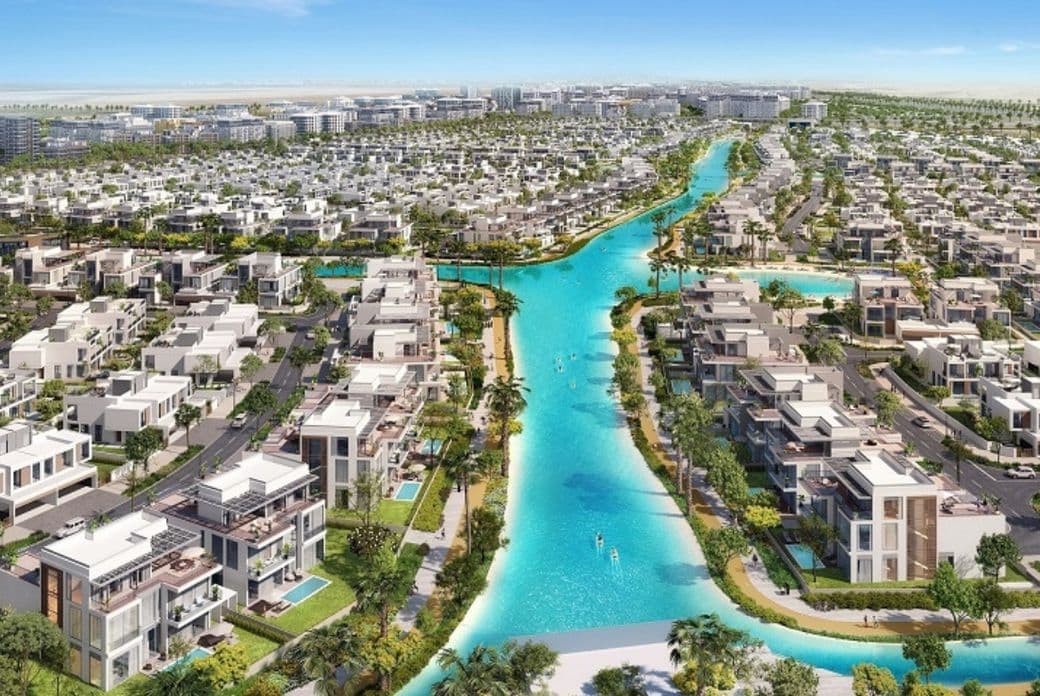 Aerial view of a residential area with modern houses, lush greenery, and a winding turquoise waterway under a clear blue sky.