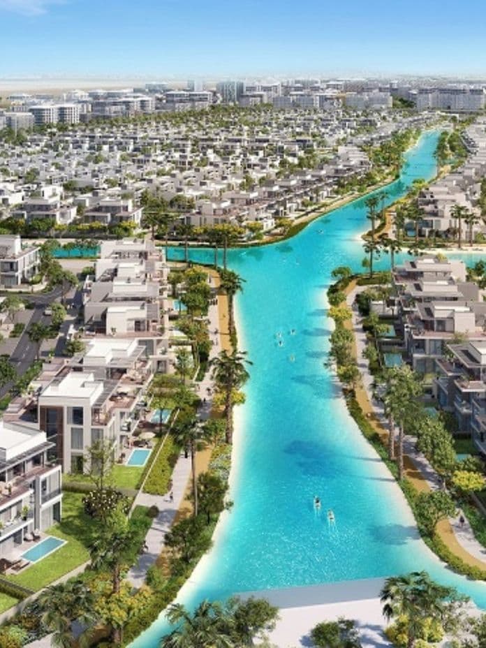 Aerial view of a residential area with modern houses, lush greenery, and a winding turquoise waterway under a clear blue sky.