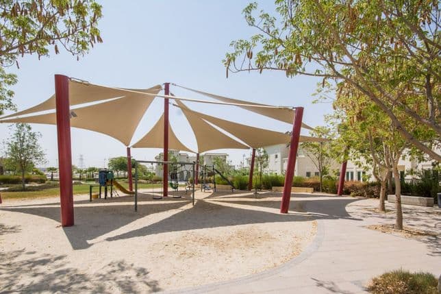 Shaded children's playground in Al Furjan featuring slides, swings, and climbing frames