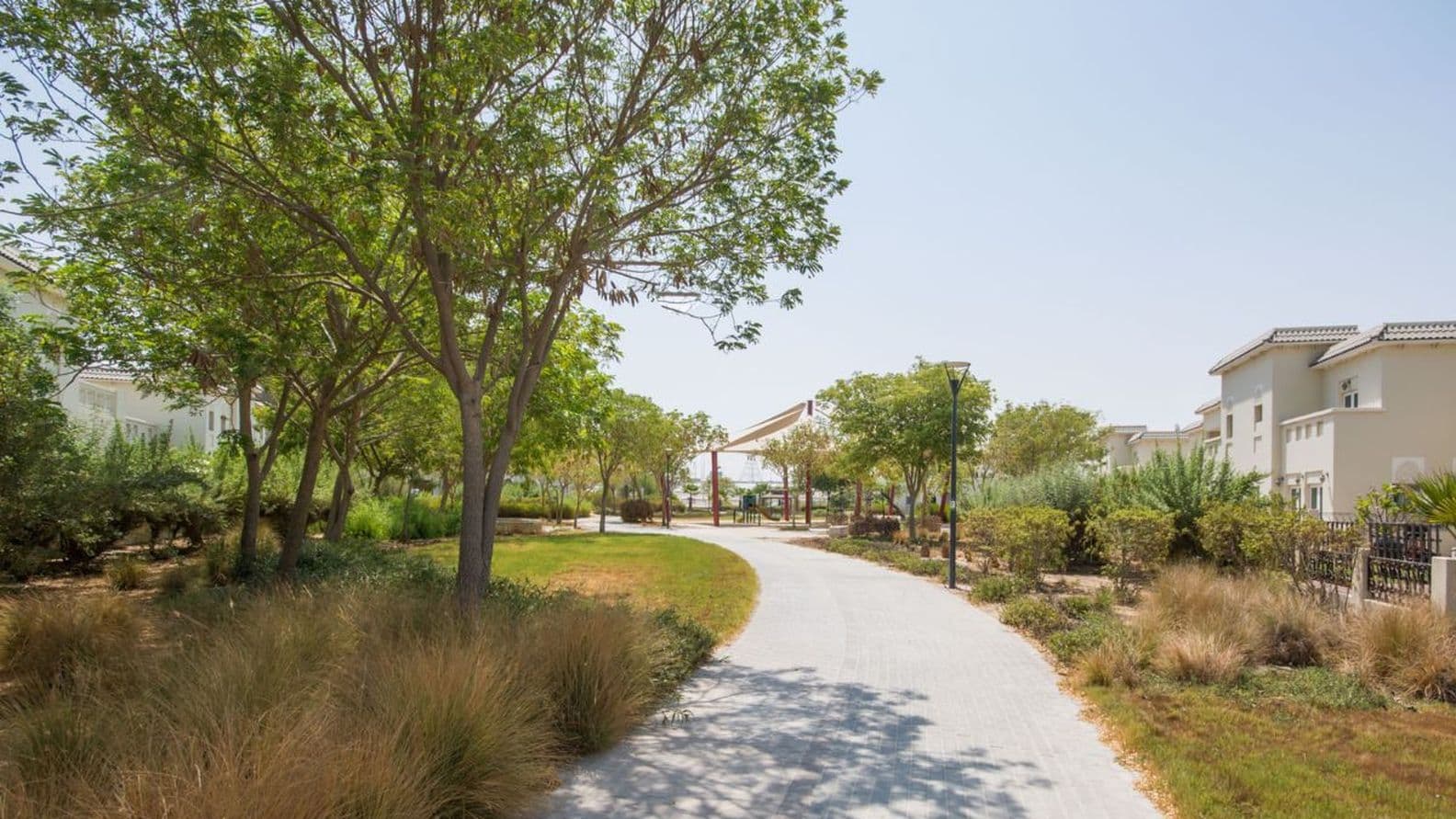 Lush green park in Al Furjan with a scenic pathway surrounded by trees and landscaped gardens.