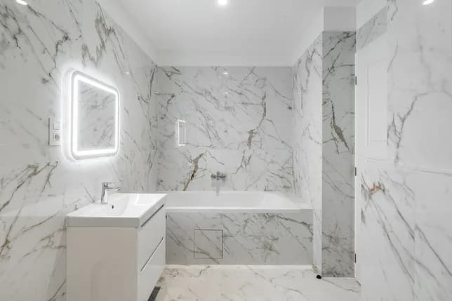 Bright bathroom with marble-effect tiles, a bathtub, white washbasin and illuminated mirror.