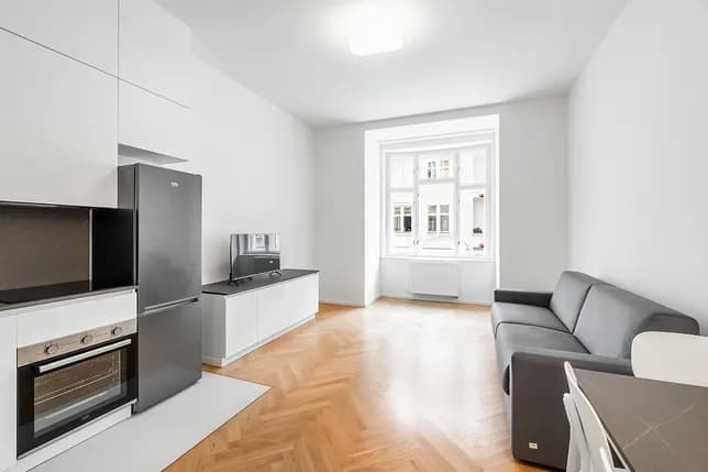 Bright living room with a modern kitchen, dining area, grey sofa and wooden parquet flooring.