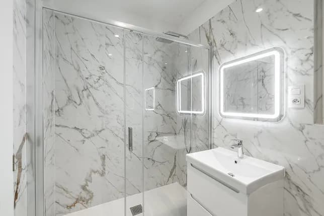 Bright bathroom with marble-effect tiles, a spacious walk-in shower, white washbasin and illuminated mirror.