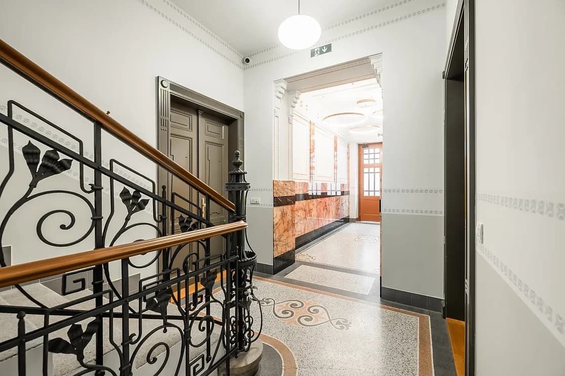 Bright interior of a historic building with decorative metal railings, original doors, terrazzo flooring and pink marble wall cladding.