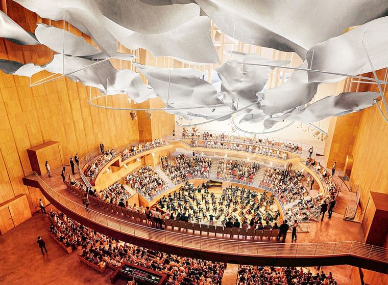 Vista interna di una sala da concerto con pareti in legno, pannelli bianchi sul soffitto e posti a sedere a gradoni pieni di persone.