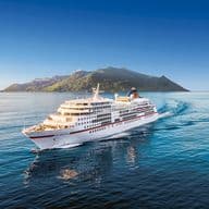 A white cruise ship, the Europa, sails on blue water near a green island under a clear blue sky.
