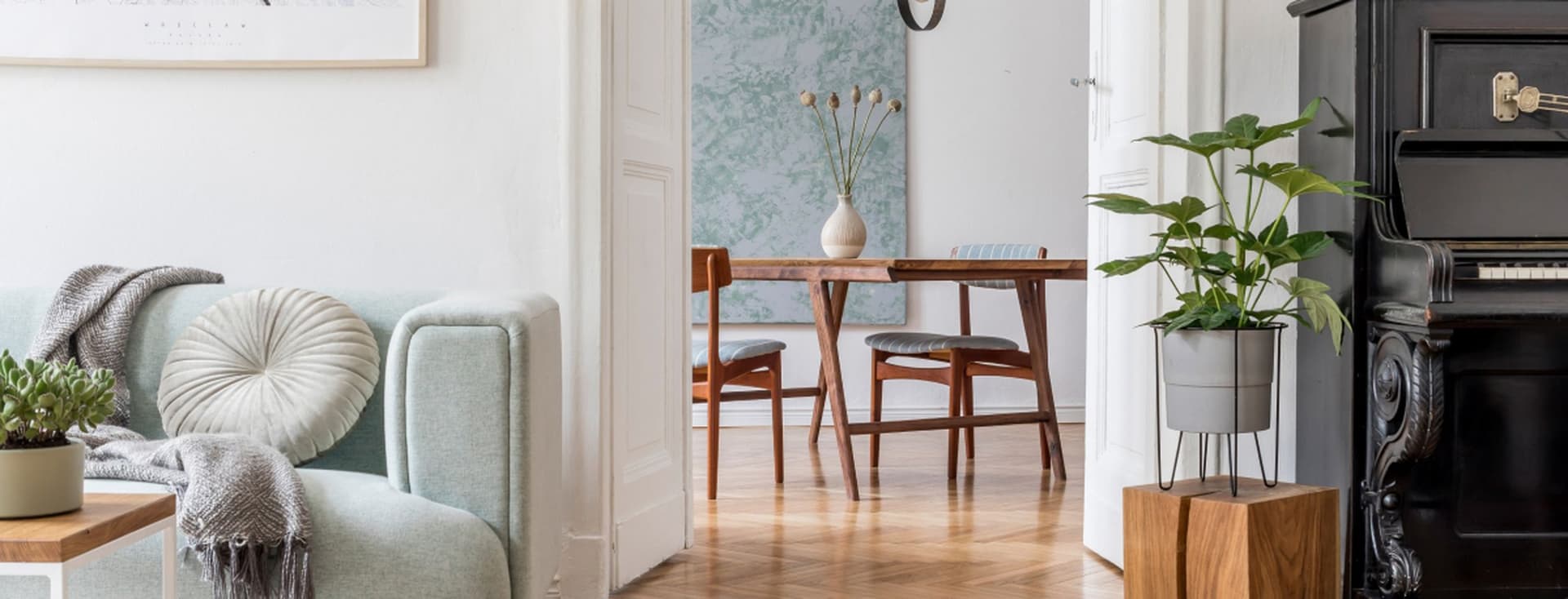 Gemütlicher Wohnbereich mit mintgrünem Akzentsessel und Decke, abstrakter Wandkunst, schwarzem Vintage-Klavier, Holzfußboden im Fischgrätmuster und modernem Essbereich, der durch die Türöffnung zu sehen ist und zeitgenössische und traditionelle Elemente miteinander verbindet