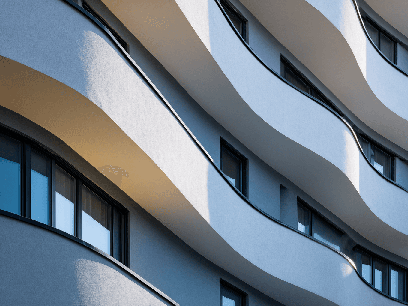 Curved, modern apartment balconies with smooth, flowing lines and shadows, featuring large windows, captured in soft lighting.