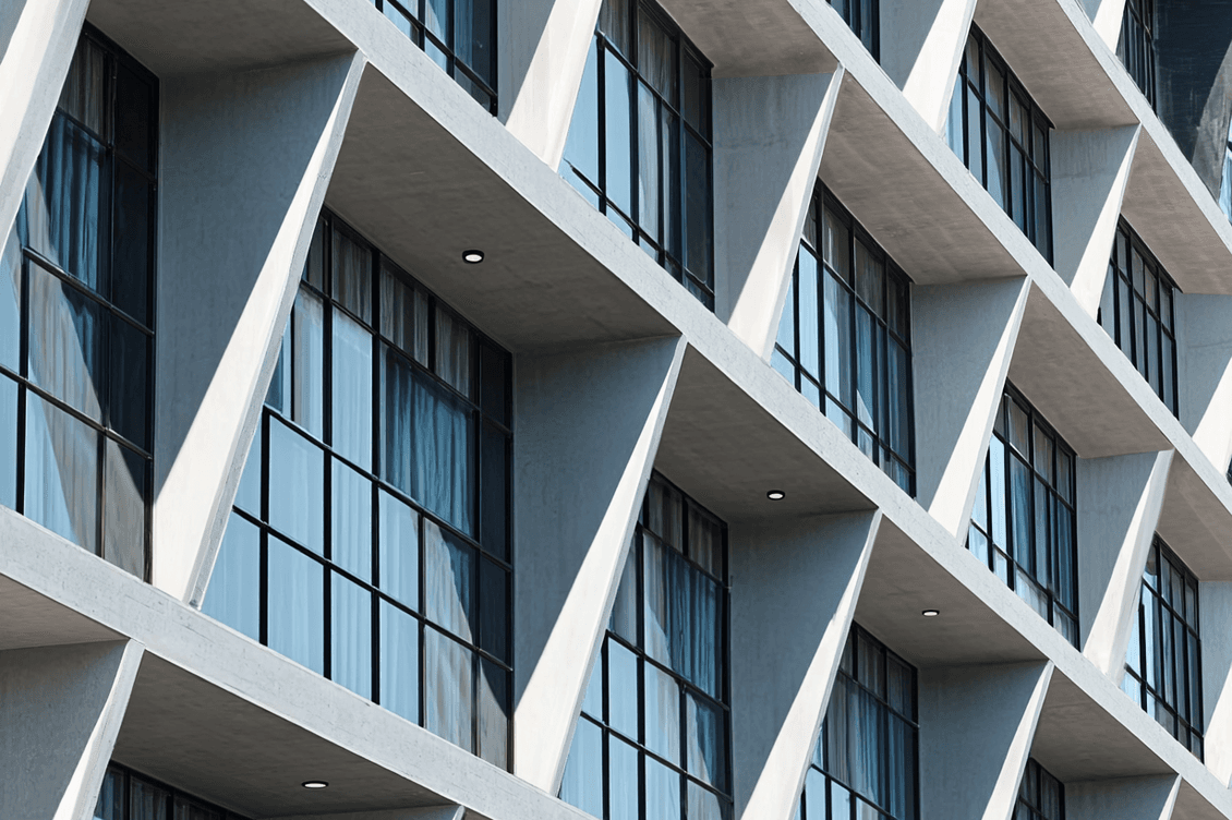 Modern building facade with diagonal concrete beams and large glass windows reflecting the sky.
