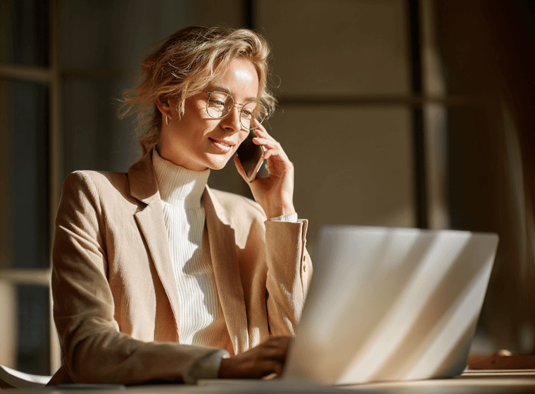 Woman talking on the phone, in front of a laptop, under direct sunlight.