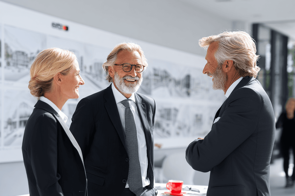 Three people in business attire having a cheerful conversation in a bright office with architectural plans on the walls.