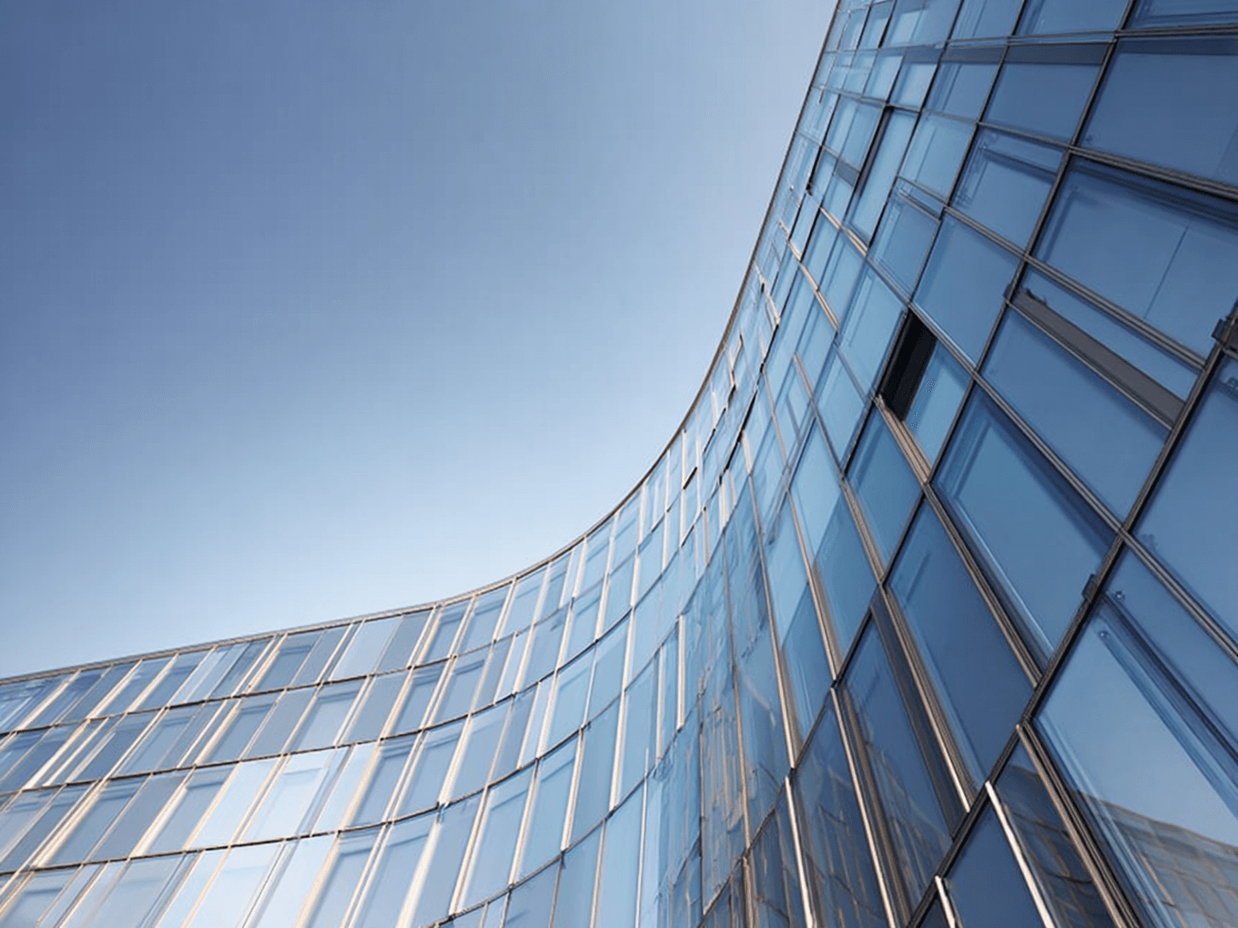 Curved modern glass building with reflective windows against a clear blue sky.