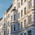Ornate white building with intricate architectural details and large windows, set against a clear blue sky.