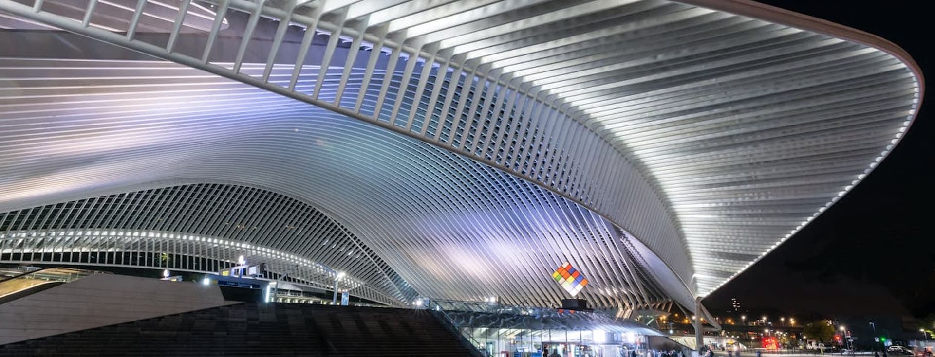 Nachtzicht op het station Luik-Guillemins, België. Het station heeft een groot, wit, gebogen dak en een plaza met mensen.