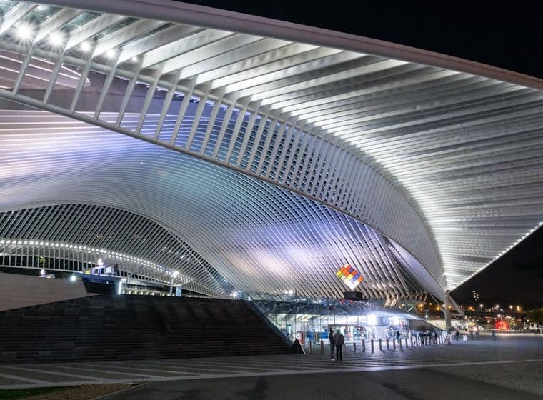 Nachtzicht op het station Luik-Guillemins, België. Het station heeft een groot, wit, gebogen dak en een plaza met mensen.
