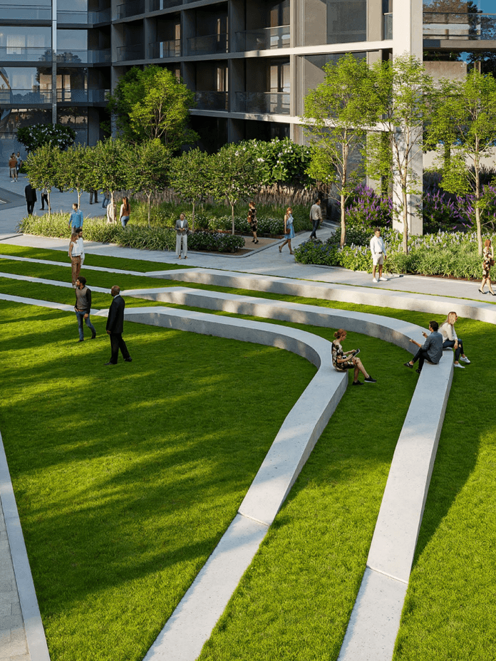 Modern urban park with tiered grass seating, surrounded by trees and people walking or sitting. Adjacent to contemporary buildings.