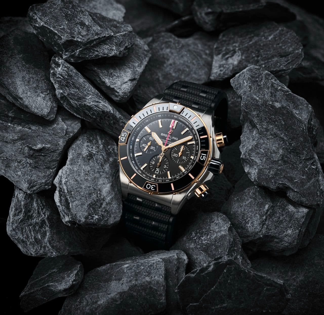 Une montre de luxe avec un cadran et un bracelet noirs est placée entre des rochers gris foncé qui mettent en valeur son design élégant et ses accents métalliques.