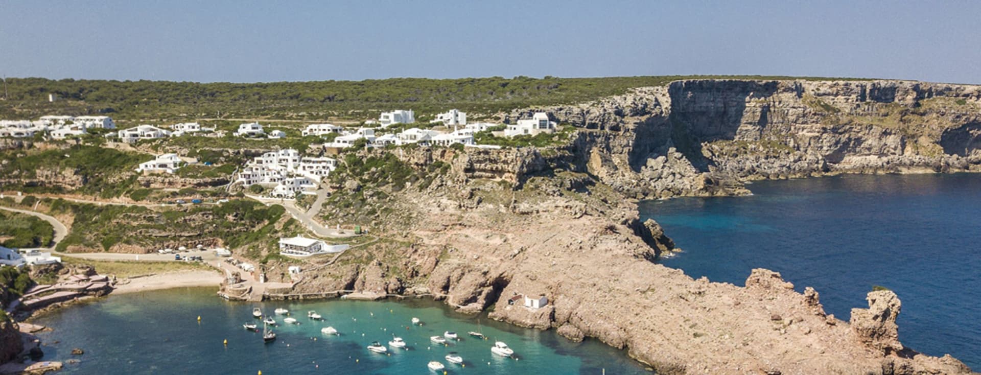 Coastal landscape with buildings on cliffs, overlooking a bay with boats.