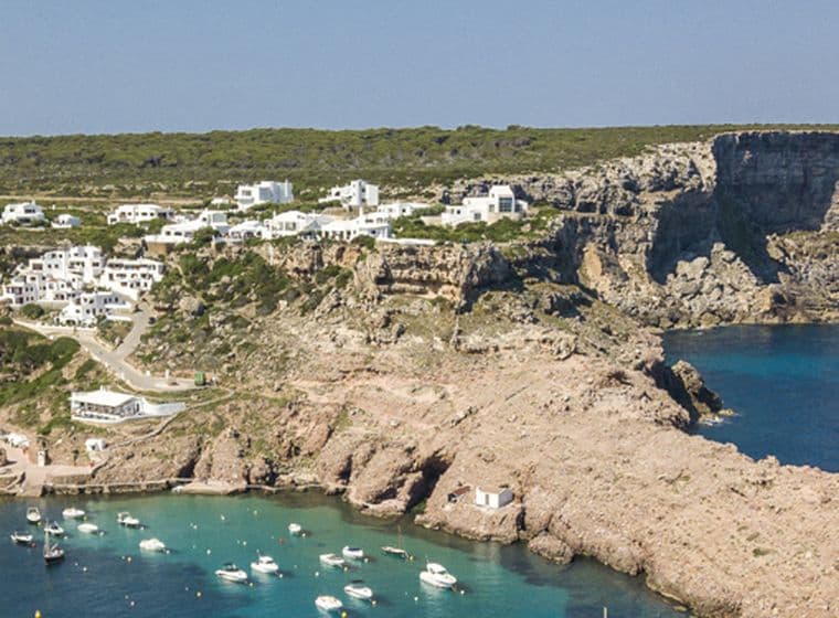 Küstenlandschaft mit Gebäuden auf Klippen und Blick auf eine Bucht mit Booten.