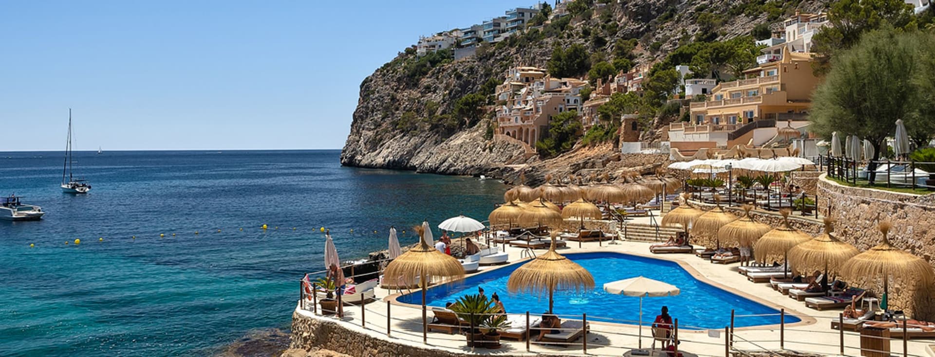 Küstenort mit Pool und Meerblick, felsigen Klippen und Booten.